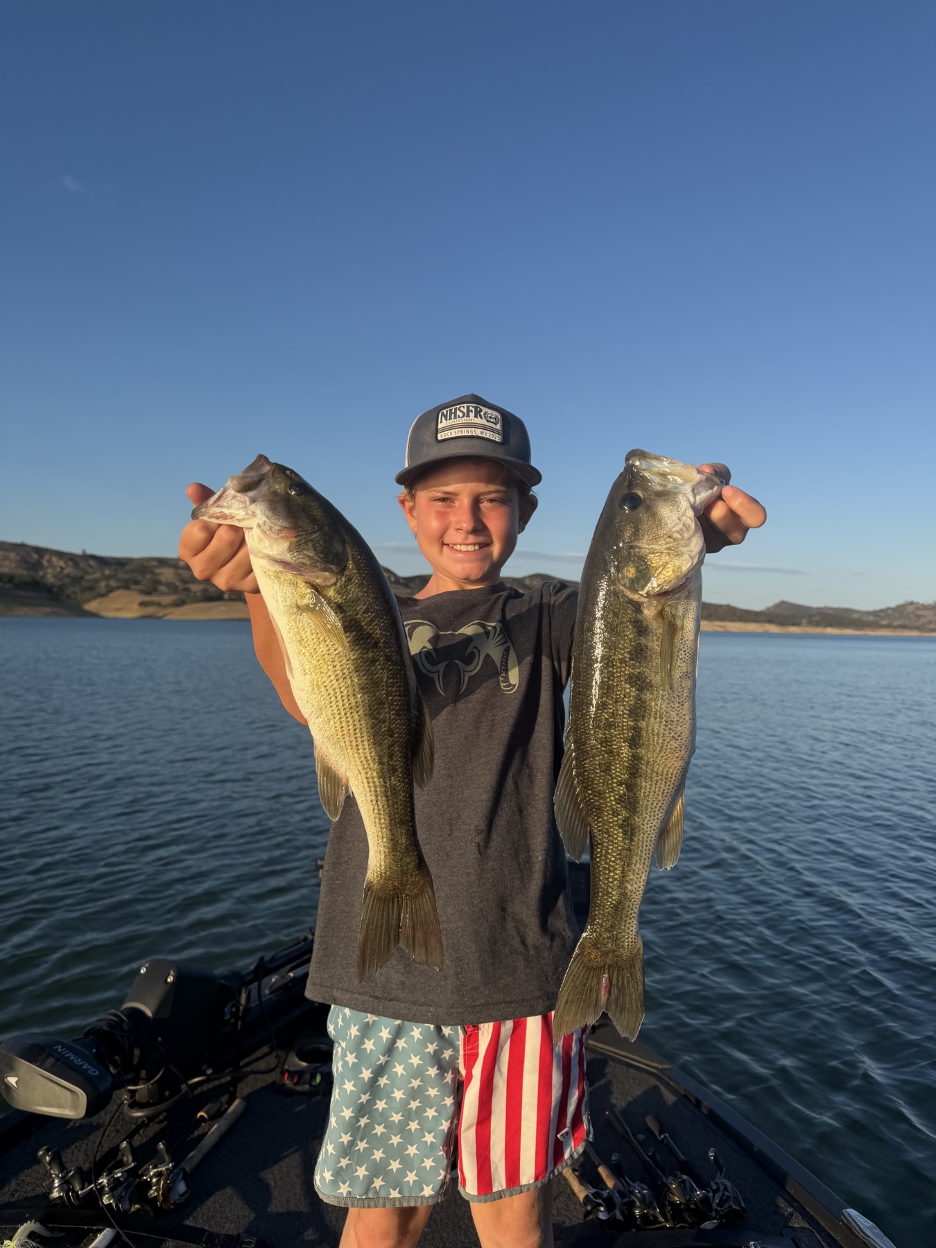 Young angler on the boat holding two largemouth bass caught on Lake Nacimiento